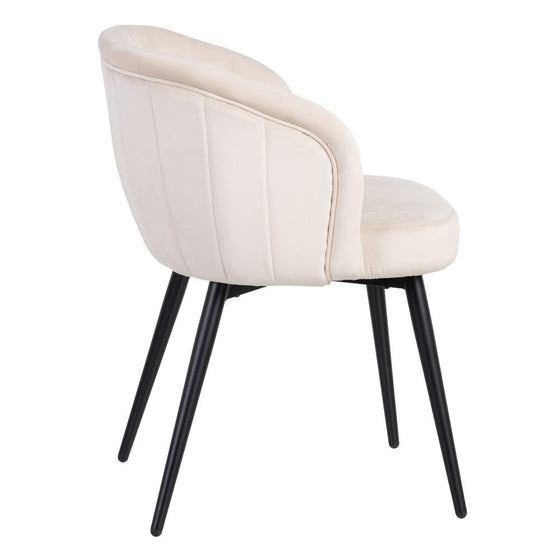 La silla de felpa beige Lusia presenta un diseño sofisticado con un respaldo curvo y patas de metal negro, visto desde el ángulo trasero izquierdo.