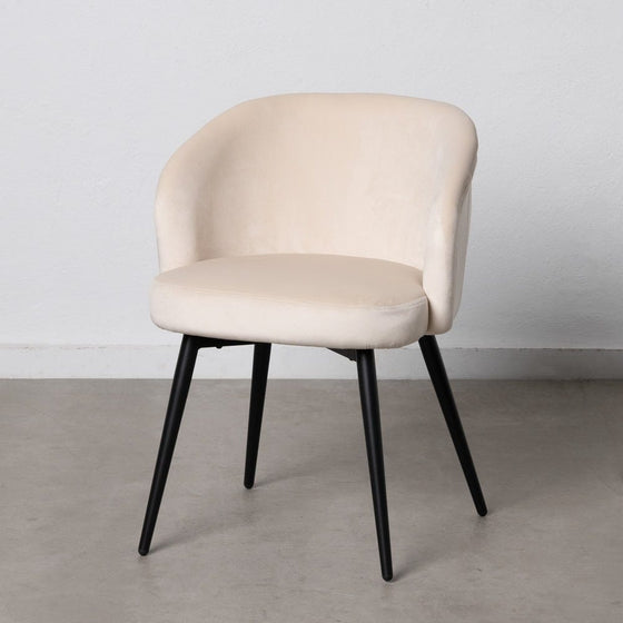 La Silla de comedor en Metal y Terciopelo Lusia, con respaldo curvo y elegantes patas de metal negro, se asienta sobre un piso de concreto gris, personificando el diseño cómodo.