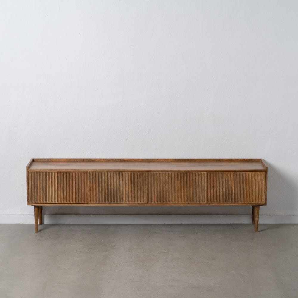 El Mueble de TV en madera de mango Apricot cuenta con ranuras verticales y cuatro patas resistentes, que exudan un diseño moderno. Se apoya elegantemente contra una pared blanca sobre un piso gris, ofreciendo una superficie lisa y elegante.