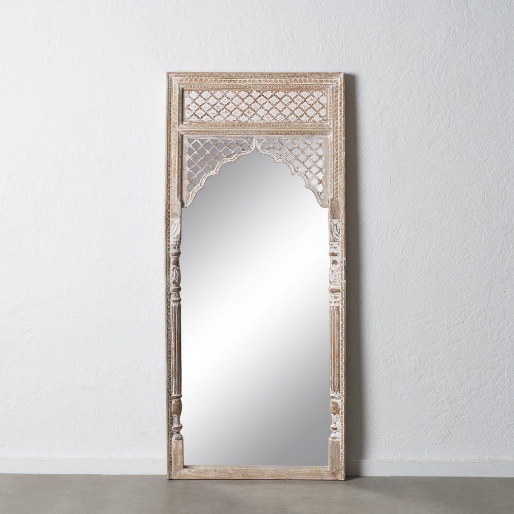 Un elegante "Espejo vestidor en madera Y DM Lgance" alto y rectangular con un marco de madera ornamentado y tallados intrincados, elaborado con rica madera de mango, se apoya elegantemente contra una pared blanca sencilla.