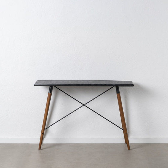 La consola en DM y metal Oslo presenta un diseño minimalista con una elegante tapa rectangular negra, patas de madera y barras transversales de metal. Fabricada con materiales de alta calidad, se destaca elegantemente contra una pared blanca sobre un piso gris claro, lo que encarna un diseño moderno.