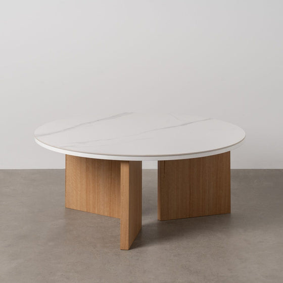 La Mesa de centro redonda Ø80 en cerámico y metal Turia presenta un diseño elegante y sencillo, con una tapa duradera sostenida por dos patas rectangulares de madera sobre una superficie gris, lo que la convierte en una adición exquisita a cualquier habitación.