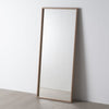 El Espejo Vestidor Madera Natural Rectangular Ayous, con su sencillo marco de madera natural, se apoya sobre una pared clara sobre un suelo liso, aportando un toque de estilo contemporáneo.