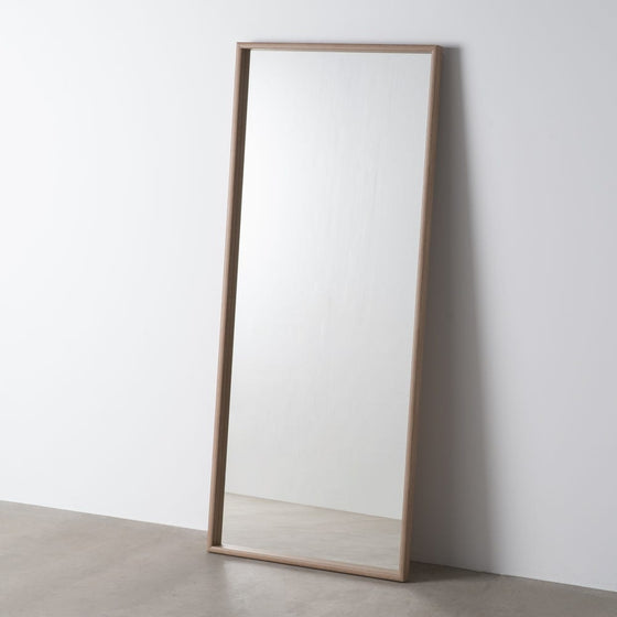 El Espejo Vestidor Madera Natural Rectangular Ayous, con su sencillo marco de madera natural, se apoya sobre una pared clara sobre un suelo liso, aportando un toque de estilo contemporáneo.