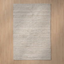  La “Alfombra en Lana y Yute Nubes” es una alfombra tejida rectangular de color gris claro sobre suelo de madera, que presenta un patrón de textura sutil y un tono neutro, ideal para una decoración contemporánea.