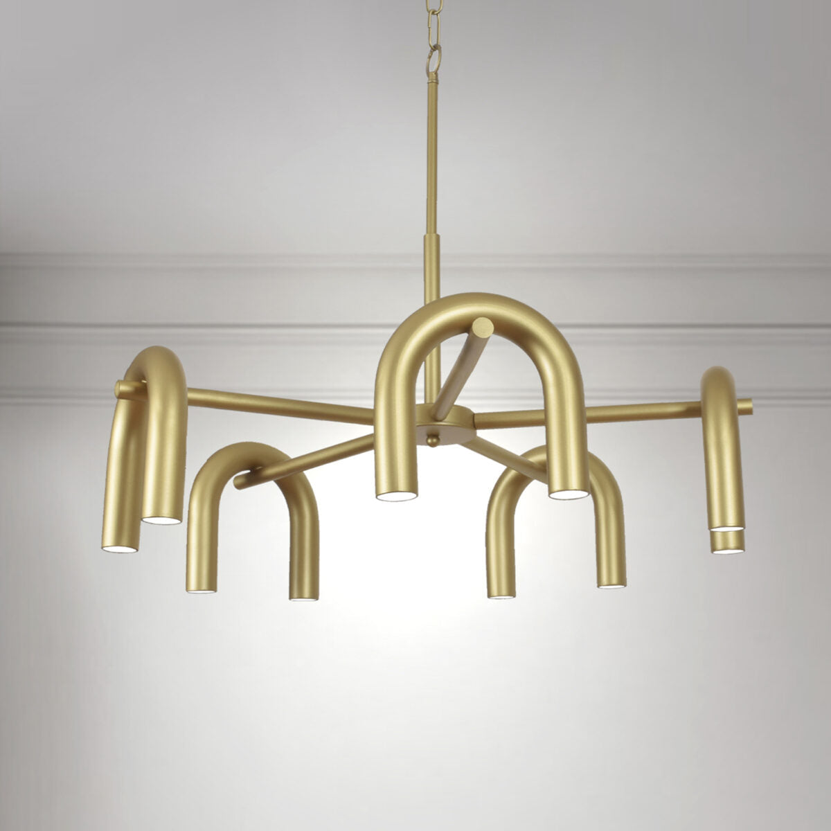 La lámpara de techo en acero X-Rhea 5 es un candelabro moderno dorado con cinco brazos tubulares curvos que sostienen luces LED, proporcionando una iluminación eficiente y brillante mientras cuelga elegantemente del techo sobre un fondo blanco liso.