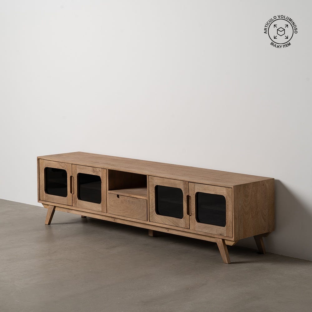 El mueble de TV de madera de mango Burnie cuenta con cuatro gabinetes con frente de vidrio y un cajón central, lo que le da un toque de diseño moderno dentro de una estética natural. Ubicado sobre un piso de concreto gris contra una pared simple, exhibe una artesanía duradera en madera de mango.