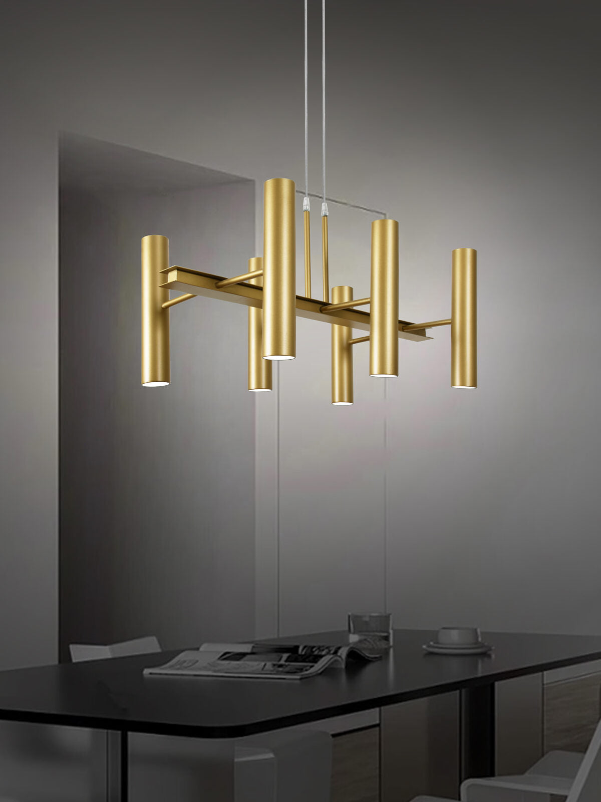 Una moderna lámpara de araña dorada cuelga elegantemente sobre una mesa de comedor oscura con un periódico y una taza, en una habitación minimalista que presenta el exquisito diseño de la Lámpara de techo en acero luz difusa Q-Toru 6.