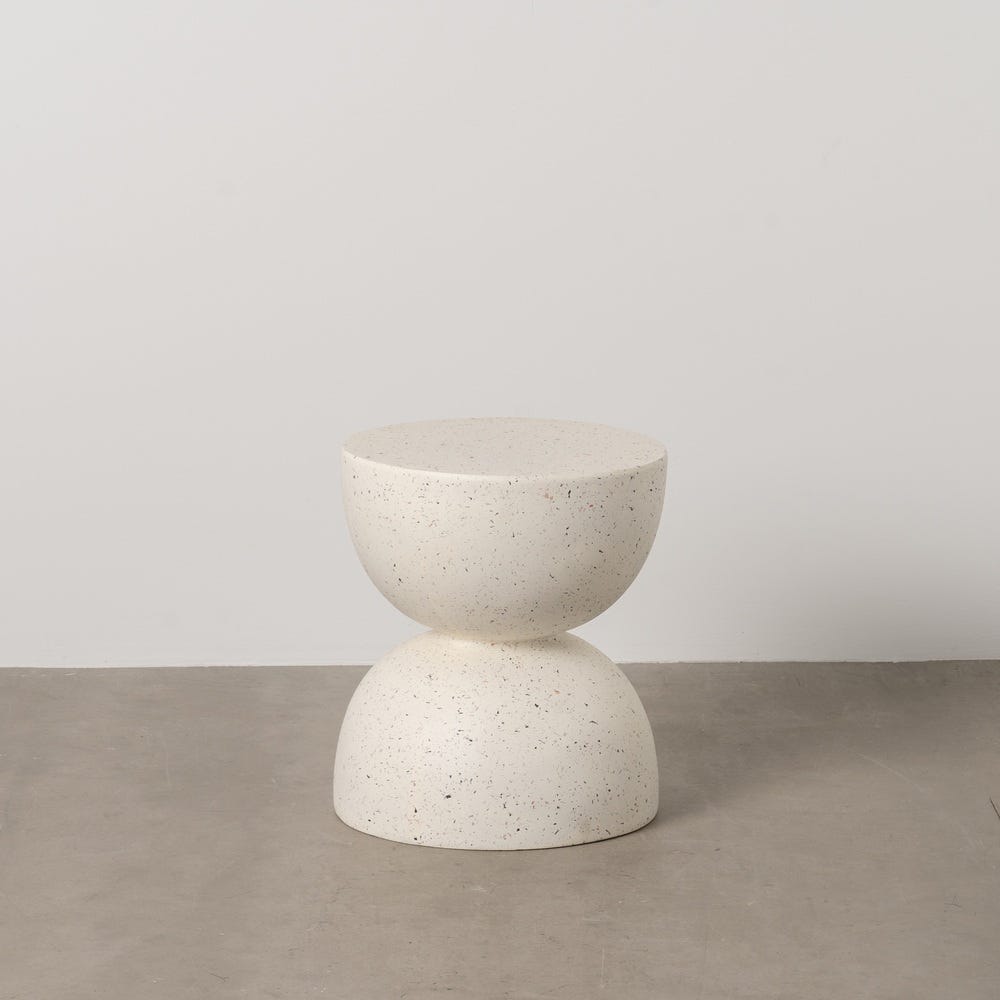 Un taburete de piedra moteada de color beige llamado "Mesa auxiliar Redonda en Fibra de magnesio Rufan Ø40" presenta un asiento y una base circulares, que descansan sobre un piso gris contra una pared blanca lisa: una encarnación del diseño moderno.