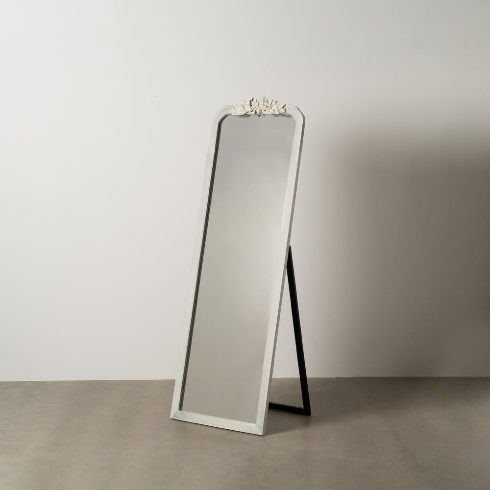 El espejo alto blanco rozado en madera de paulonia de Lumis presenta un diseño vintage ornamentado y se alza elegantemente sobre un soporte negro simple. Colocado contra una pared clara, agrega encanto y crea una atmósfera acogedora.