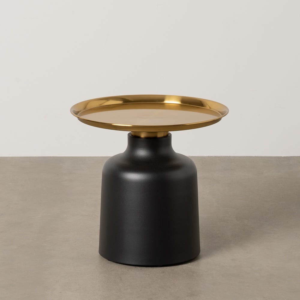 La Mesa auxiliar en metal negro dorado Vetal Ø50 cuenta con una base negra y un tablero dorado, elegantemente colocados sobre un suelo de hormigón gris.