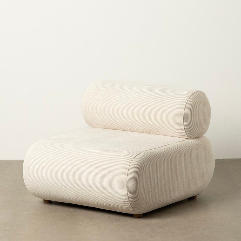 El Sillón en Madera de Abedul y Tejido Pana Broto, un sillón minimalista y moderno de color beige con bordes redondeados y respaldo cilíndrico, elaborado con materiales de alta calidad, reposa elegantemente sobre un piso gris liso contra una pared blanca.