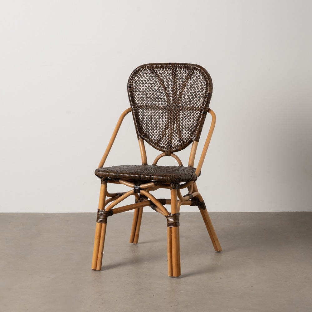 La silla de comedor en madera Berne, una silla de ratán con respaldo y asiento de tejido, muestra un estilo contemporáneo. Su estructura de bambú de color claro irradia elegancia natural mientras reposa con gracia sobre un piso de concreto liso contra una pared blanca.