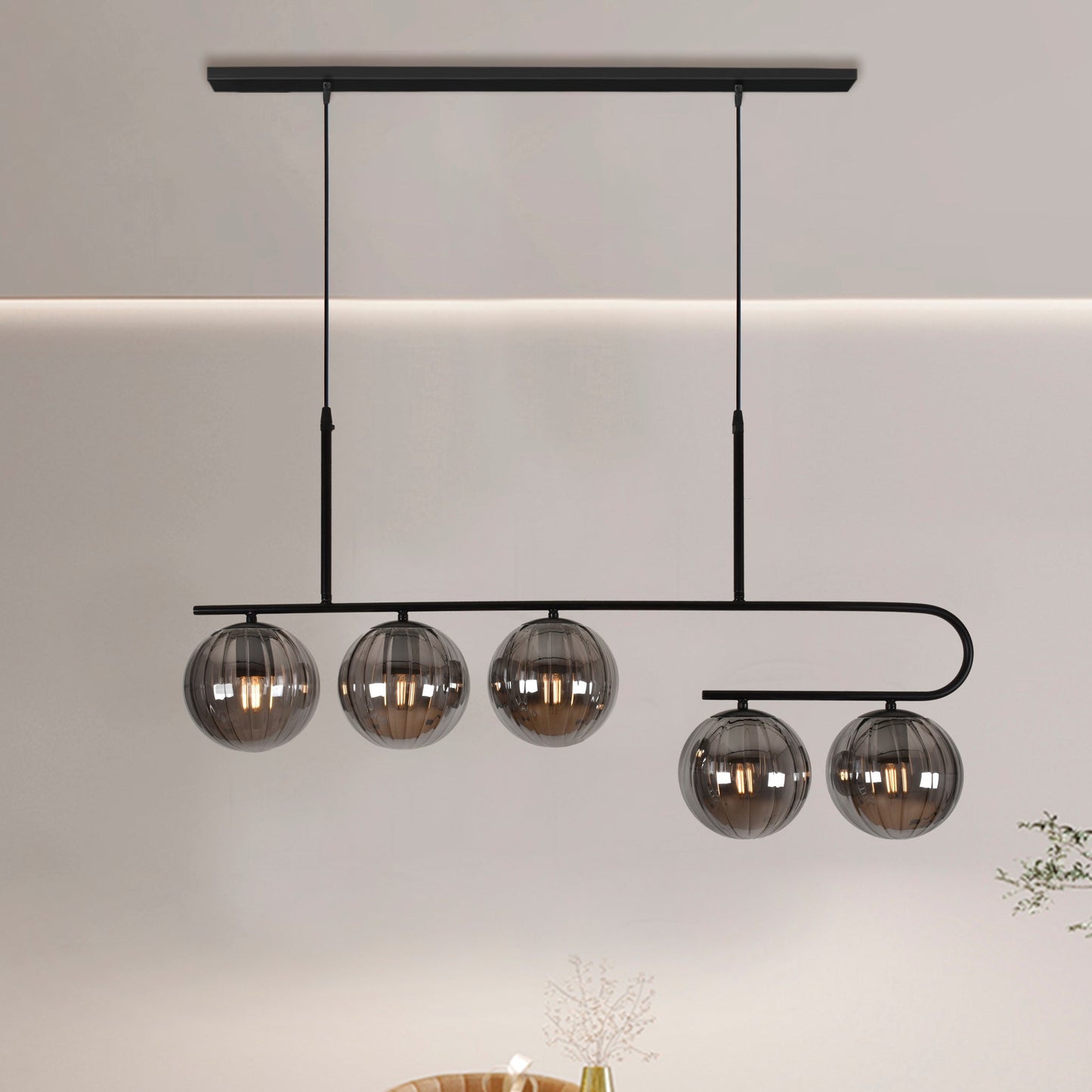 La lámpara de techo en acero negra Ball 7 presenta cinco pantallas esféricas de vidrio elegantemente suspendidas de su marco, creando un diseño contemporáneo sorprendente contra una pared neutra.