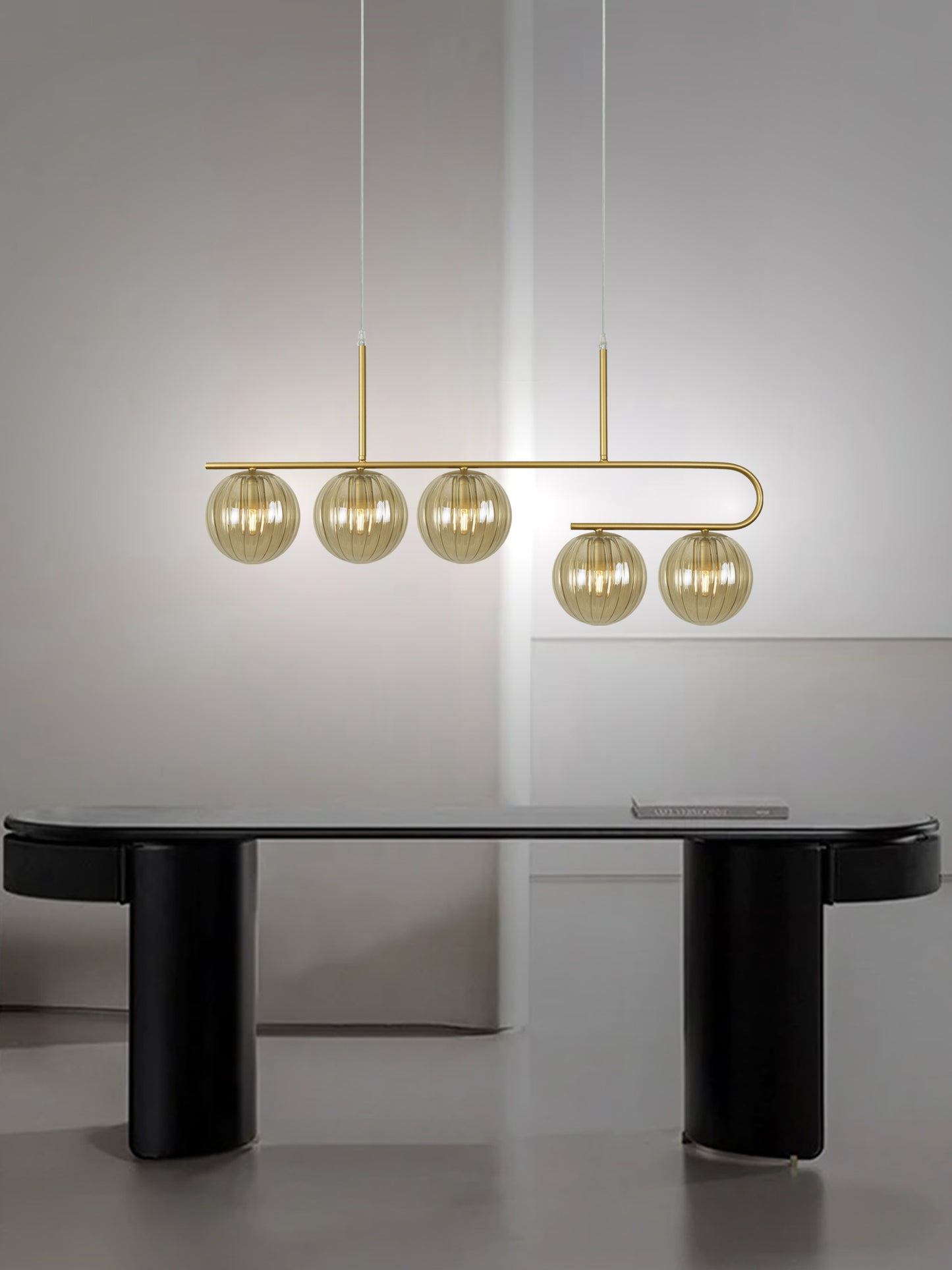 Una habitación moderna con un elegante escritorio negro y una lámpara de techo en acero negra contemporánea Ball 7, con cinco bombillas esféricas en tonos dorados, colocadas contra una pared gris minimalista para exhibir un exquisito diseño contemporáneo.