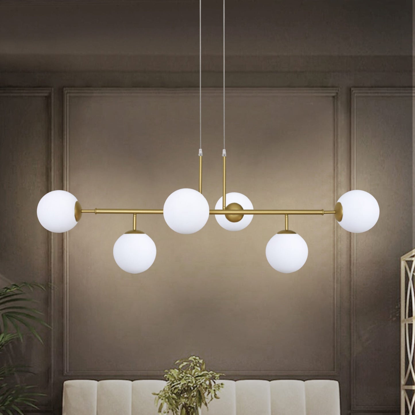 La elegante lámpara de techo Line Ball 6 con marco dorado y seis luces blancas redondas adorna la habitación, complementando la pared gris y la planta.