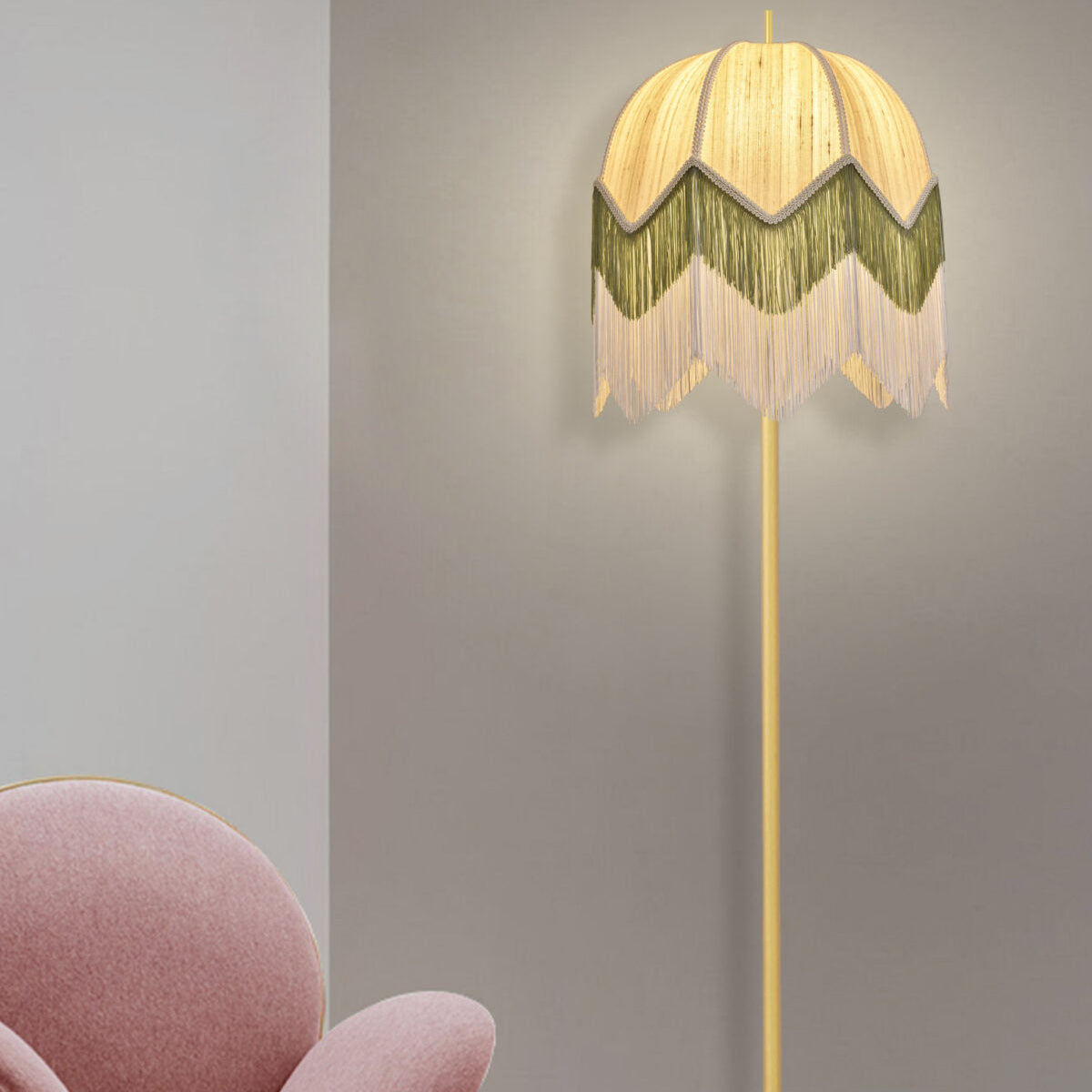 La Lámpara de pie vintage de flecos Zelena se coloca junto a una silla tapizada en rosa contra una pared gris claro, aportando un toque de decoración interior y proporcionando una iluminación cálida.