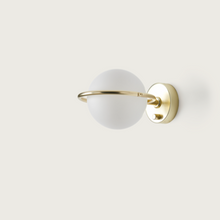  La lámpara de pared Abbacus presenta una pantalla esférica de vidrio esmerilado con un anillo de metal dorado, montada sobre una base circular dorada, que ofrece un diseño elegante y encarna una iluminación minimalista.