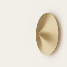  Una decoración minimalista de pared ovalada dorada que presenta un diseño geométrico dentado e iluminación funcional, sobre un fondo blanco liso.