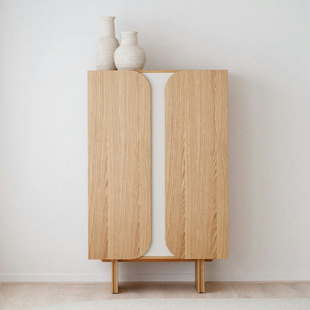 El Armario Moderno Roble Natural con Estantes - Curva presenta un diseño minimalista, se apoya contra una pared blanca y está rematado con dos jarrones de cerámica blanca.