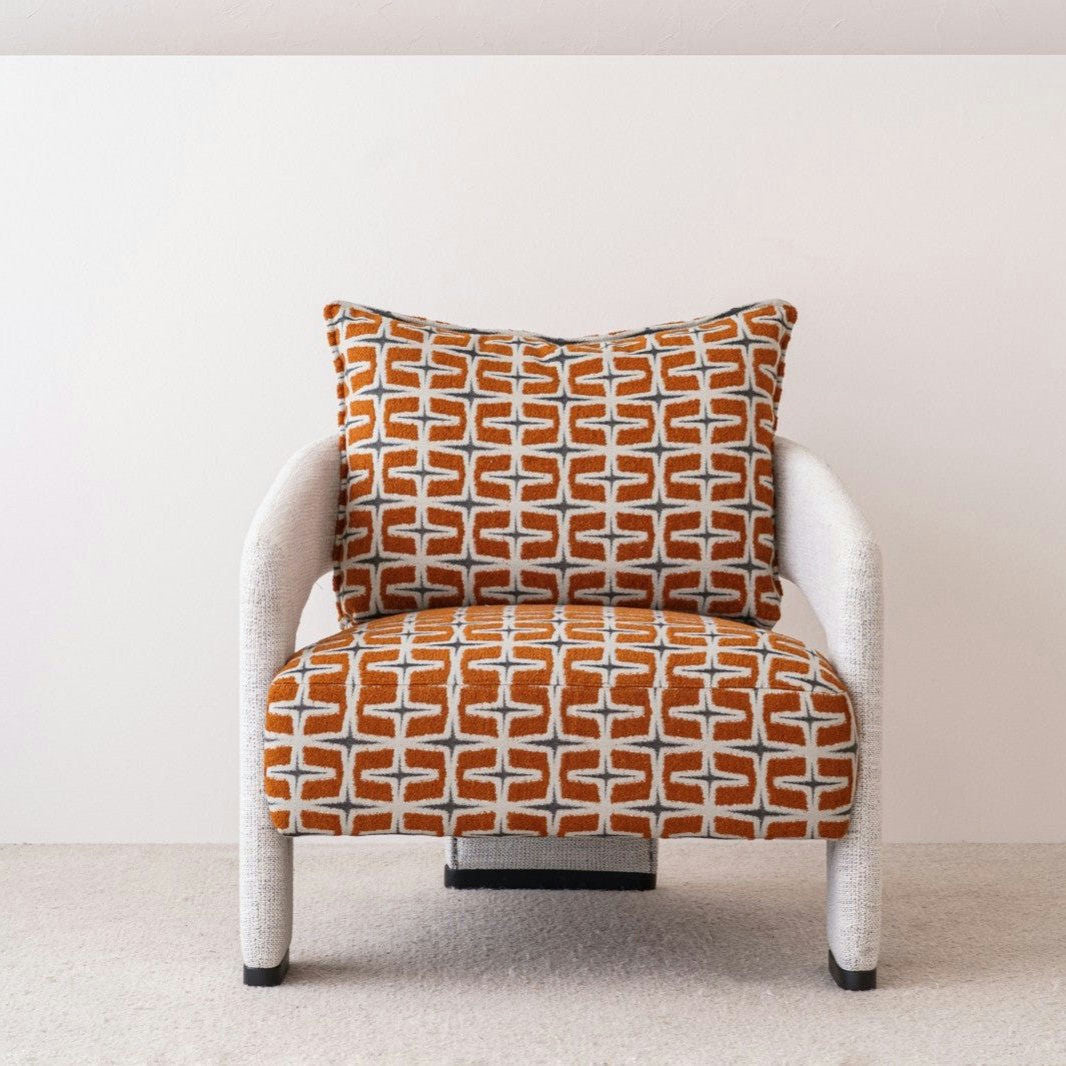 La Butaca Tapizada en Beige y Naranja Doble es una butaca moderna con estructura blanca y cojín con motivos geométricos de color naranja, realizado en 100% poliéster, sobre un fondo blanco liso.