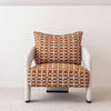 La Butaca Tapizada en Beige y Naranja Doble es una butaca moderna con estructura blanca y cojín con motivos geométricos de color naranja, realizado en 100% poliéster, sobre un fondo blanco liso.