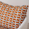Una almohada geométrica naranja reposa sobre una Butaca Tapizada en Beige y Naranja Doble, resaltando su diseño contemporáneo.
