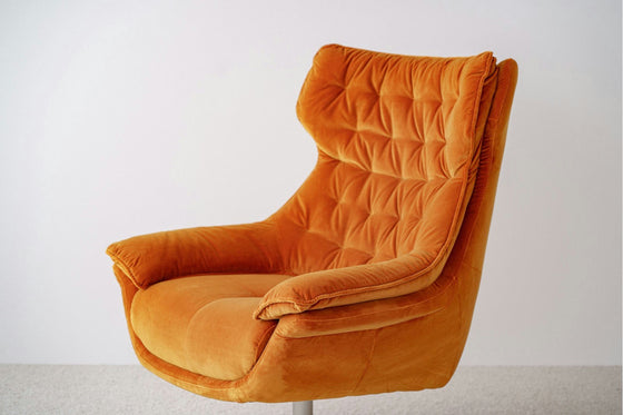La Butaca Giratoria Tapizada en Terciopelo Naranja presenta una tapicería capitoné y un respaldo alto, que encarna el mobiliario elegante y el diseño moderno, sobre un fondo blanco liso.
