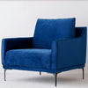 La Butaca en Terciopelo Azul Noche Helia, con elegantes patas de metal, personifica el estilo de interiorismo. Ubicado lujosamente sobre una alfombra clara, rezuma lujo y comodidad.