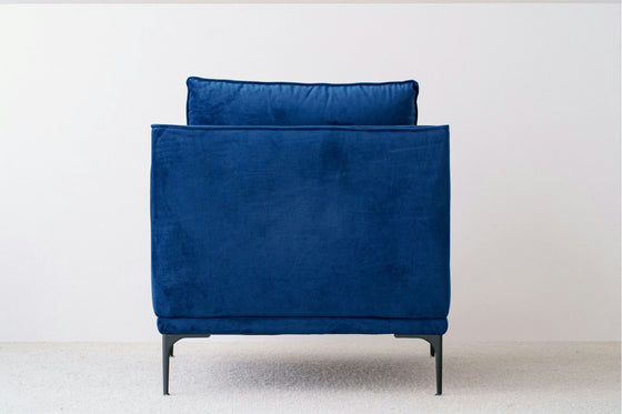 La Butaca en Terciopelo Azul Noche Helia, con un respaldo acolchado de felpa, combina lujo y comodidad a la perfección. Sus esbeltas patas negras contrastan elegantemente con alfombras claras y paredes blancas y lisas, realzando cualquier estilo de interiorismo.