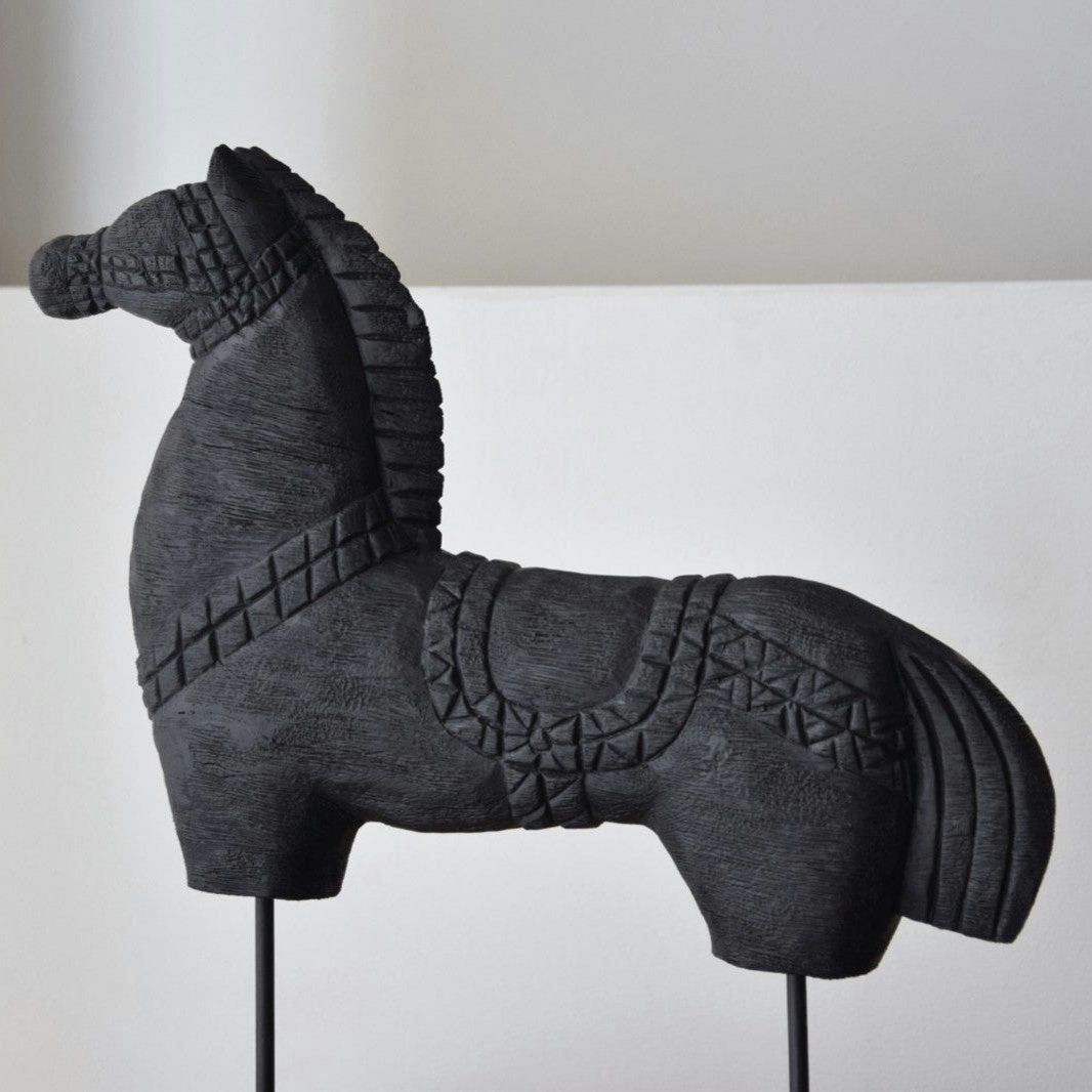 La Figura Decorativa en Madera Tallada Caballo N.3, intrincadamente tallada, es una figura de caballo de madera de mango gris oscuro con una superficie bellamente texturizada, elegantemente mostrada sobre un fondo liso.