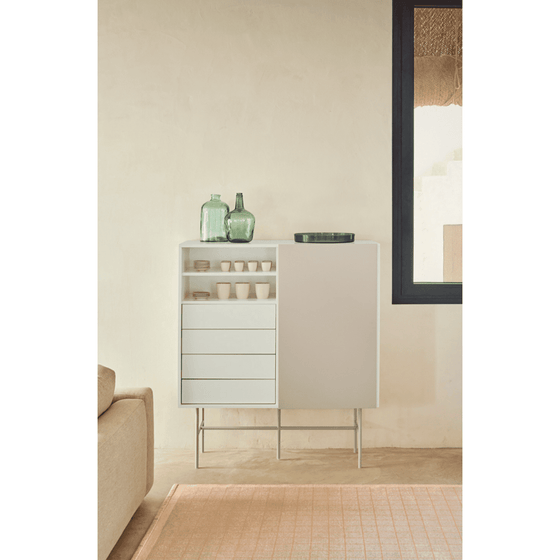 Un Mueble Auxiliar Nube 1P4C con cajones en una habitación minimalista, diseñado para la funcionalidad y rematado con botellas de vidrio verde y tazas blancas.