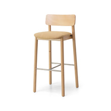  El Taburete Alto en Madera y Tapizado Bion AT destaca por su diseño minimalista con una estructura de madera de haya. Este taburete cuenta con un asiento y respaldo acolchonados en tono marrón claro, cuatro patas, un respaldo rectangular y reposapiés metálicos.