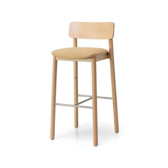 El Taburete Alto en Madera y Tapizado Bion AT destaca por su diseño minimalista con una estructura de madera de haya. Este taburete cuenta con un asiento y respaldo acolchonados en tono marrón claro, cuatro patas, un respaldo rectangular y reposapiés metálicos.