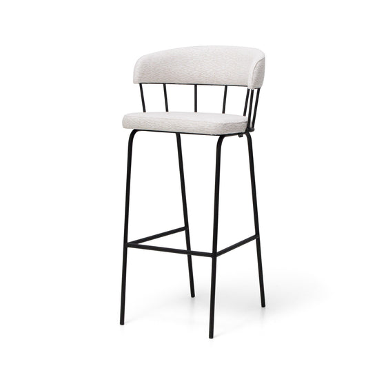 El Taburete Alto en Metal y Tapizado Yasmina es un taburete alto con asiento acolchado y respaldo ligeramente curvado, que presenta un diseño moderno y elegante con patas de metal negro y tapizado en tela ligera.