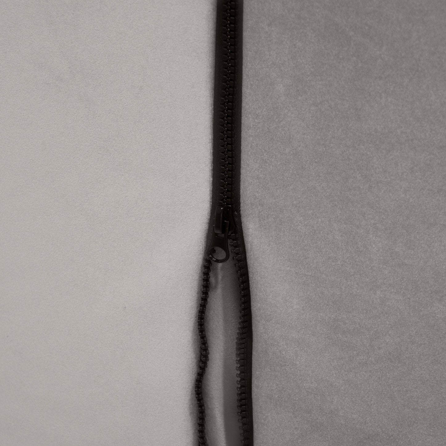 Un primer plano de una cremallera negra parcialmente abierta sobre tela gris muestra la suave textura del Bean bag puff de terciopelo 115×90×75 cm - CLIP CLAP 115 BARCELONA, ideal para salones o dormitorios modernos.