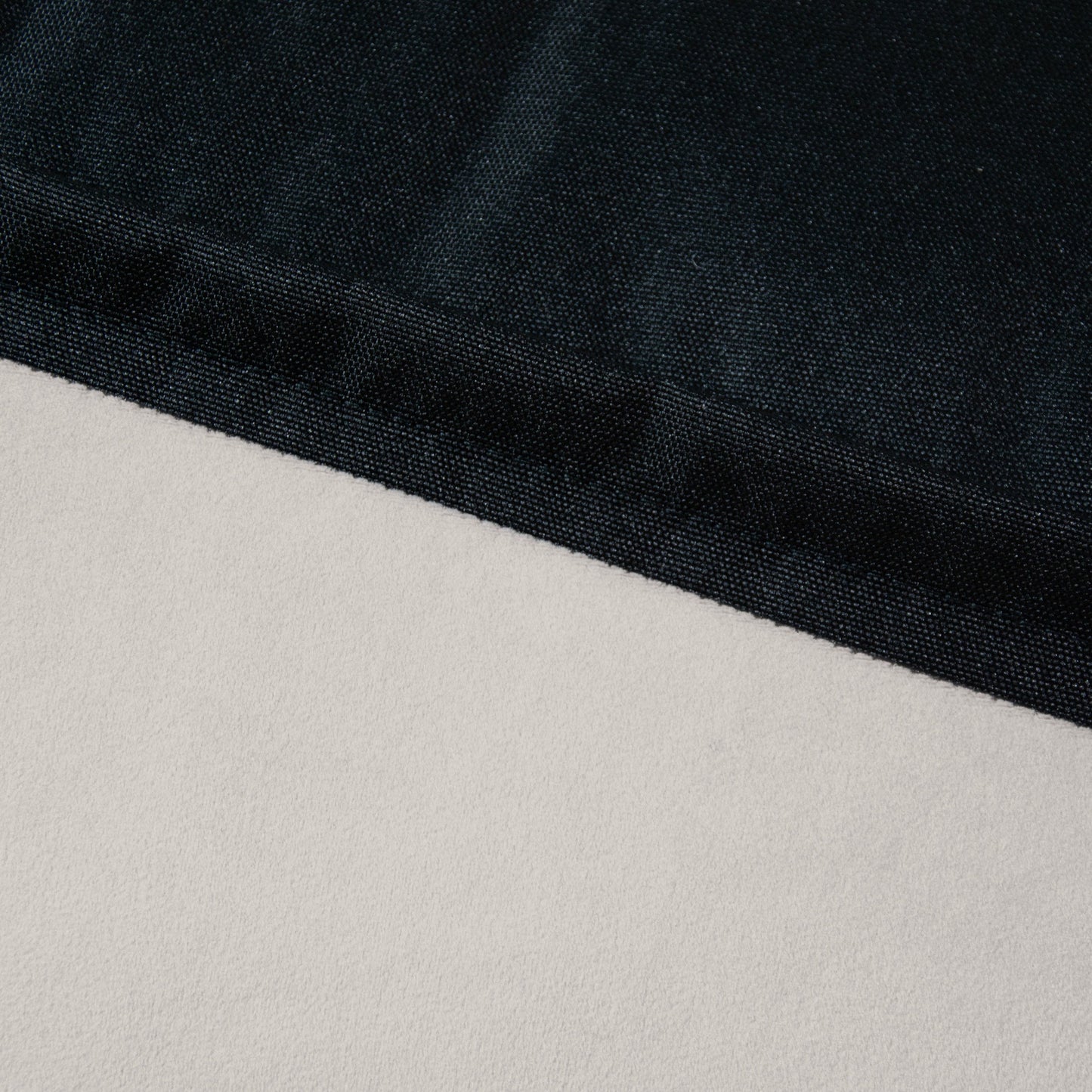 Primer plano del puff de terciopelo CLIP CLAP 115 BARCELONA (115×90×75 cm), en el que se aprecia el contraste entre las superficies texturizadas en negro y lisas en gris claro, sello distintivo de su moderno diseño para salón o dormitorio.