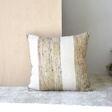  Cojín Algodón Tostado y Blanco Ares N.5, una almohada cuadrada con rayas beige y blancas hecha de 100% algodón, se coloca elegantemente sobre una alfombra gris claro contra un panel de madera.