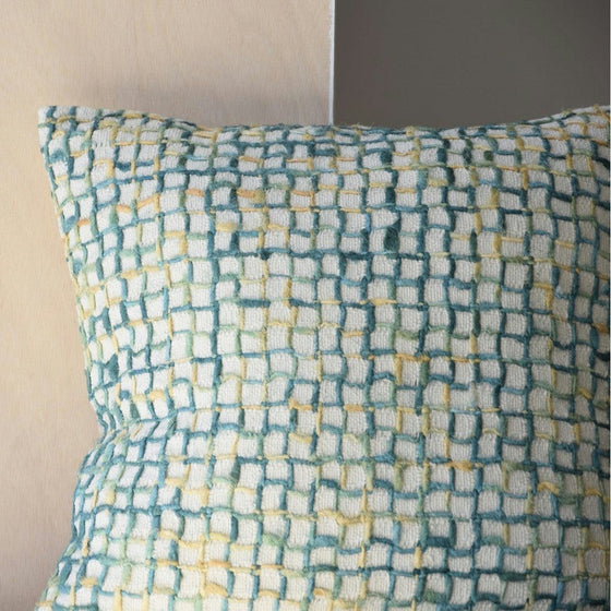 El cojín Algodón Verde Blanco. Vega N.2, con un estampado de cuadros verdes, amarillos y crema, reposa sobre una pared clara y aporta un toque moderno a la decoración interior.
