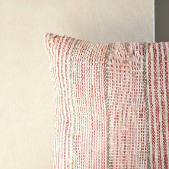 Primer plano de un Cojín Mara N.4 en Algodón Tostado y Rojo con rayas verticales rojas y beige sobre un fondo de madera clara, perfecto para diseño de interiores.