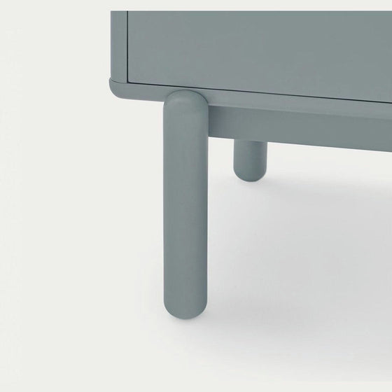 Primer plano de una pata de mesa lisa y cilíndrica de color gris de la Cómoda en MDF y Roble con 4 Cajones Corvo 4C con diseño moderno, apoyada sobre una superficie clara.