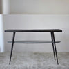 La Consola Lena Metal Negro Mármol Verde es una mesa consola moderna que realza cualquier decoración contemporánea con su tablero de madera y estructura de metal, combinados con un estante inferior de vidrio. Colocada sobre una alfombra clara, agrega elegancia a cualquier habitación.