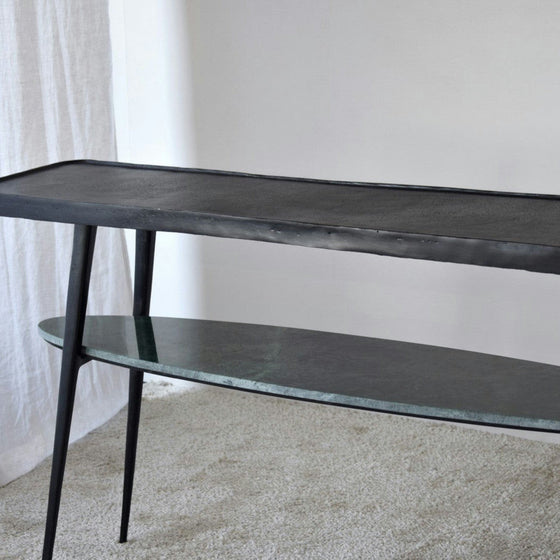 La consola Lena Metal Negro Mármol Verde tiene una estructura de metal negro, una parte superior rectangular y un estante inferior ovalado. Combina bien con alfombras claras y detalles de mármol verde para darle un toque elegante y contemporáneo a tu espacio.