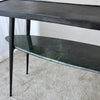 La Consola Lena Metal Negro Mármol Verde es una mesa negra de dos niveles que presenta un tablero rectangular delgado y un estante inferior de mármol verde, que se coloca elegantemente sobre un piso alfombrado y encarna una decoración contemporánea.