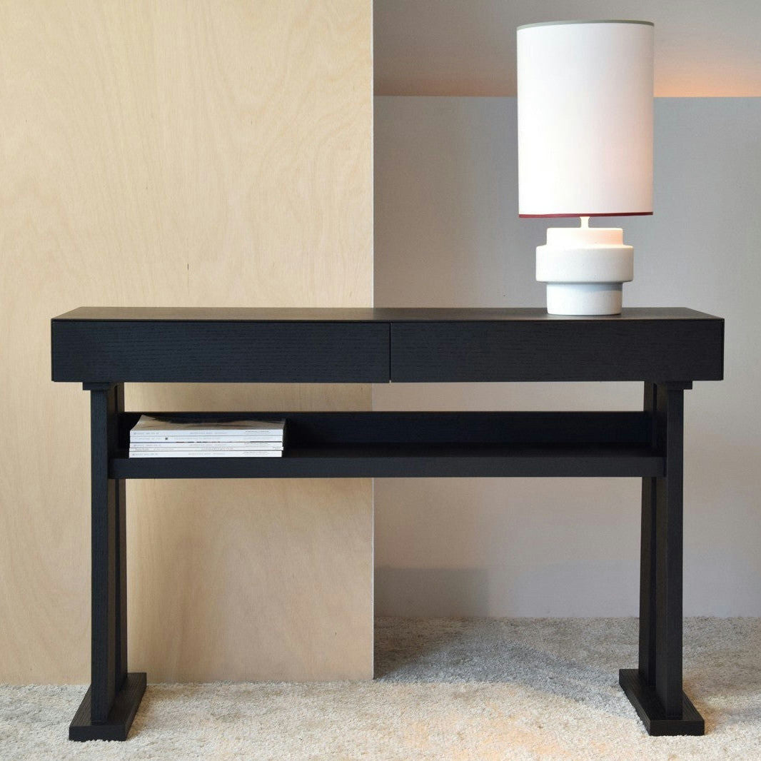 Consola Roble Negro Mate - Estilo Loft, con cajón y estante inferior, para revistas sobre un piso alfombrado. Una moderna lámpara blanca completa el diseño minimalista de esta elegante consola negra.