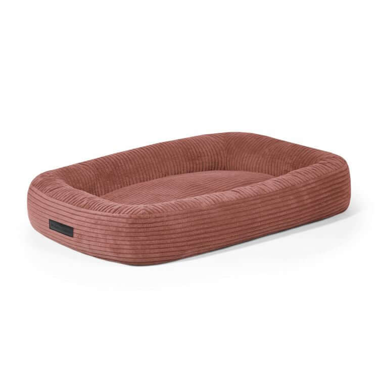 La Cama para perro de terciopelo acanalado 75×60×18 cm - DOG BED 75 WAVES, rectangular y de color rosa con bordes en relieve y superficie plana, se muestra sobre fondo blanco. Ideal como cama hipoalergénica para perros.