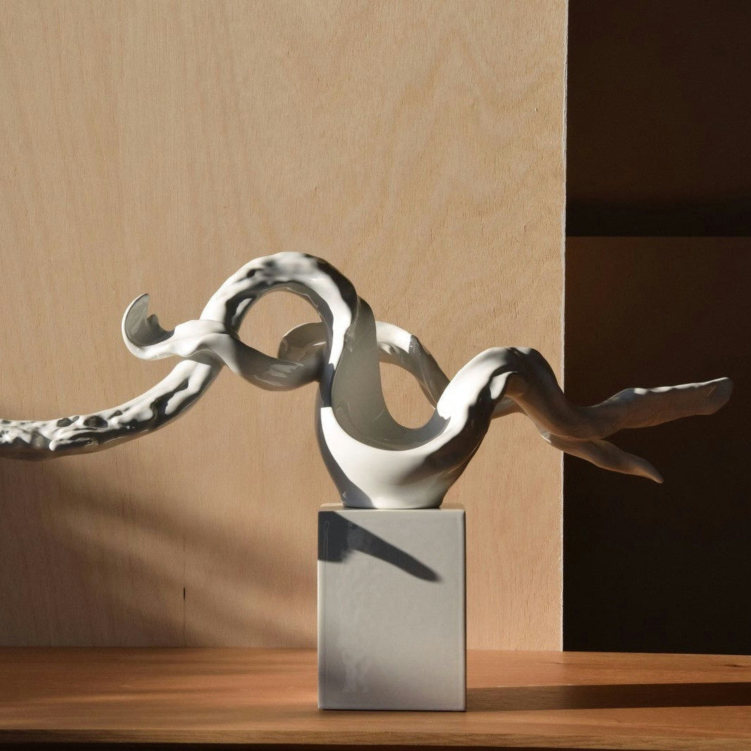 La Escultura Abstracta Rama Cerámica Blanco - Elegancia Zen presenta formas alargadas y retorcidas sobre un pedestal rectangular con un fondo con textura de madera. Esta notable pieza de Arte Contemporáneo eleva sin esfuerzo cualquier espacio centrado en Decoración e Interiorismo.