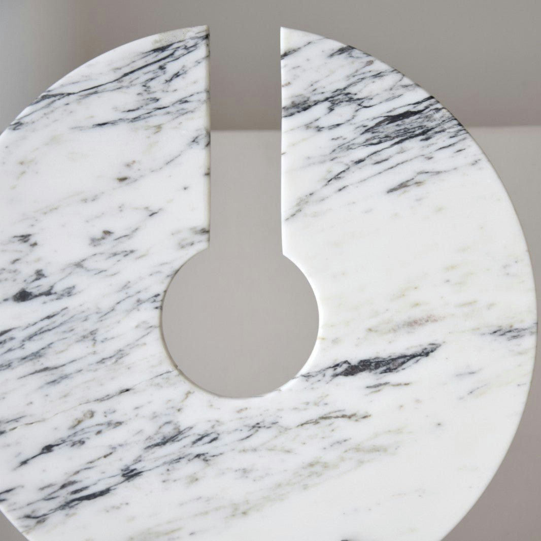 Primer plano de Escultura Arnela N2. Mármol y Metal circular con corte en forma de cuña. Ideal para decoración de interiores, presenta vetas grises y negras en su superficie de mármol suave y pulido.