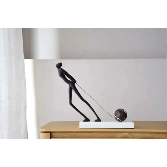 Una Escultura Arrastre de un hombre con una bola encima de una mesa. Metal y Mármol.