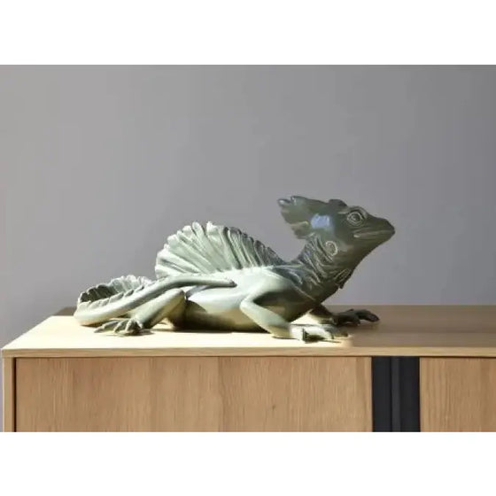 Una escultura de cerámica basilisco verde descansa sobre un gabinete de madera en el hogar.